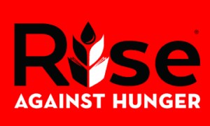 Volunteers at Good Shepherd Austin packaging meals together for the Rise Against Hunger event — tables full of bags, rice, and supplies ready for assembly.