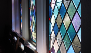 Colorful stained glass windows inside Good Shepherd Episcopal Church in Austin, Texas, featuring a diamond-patterned design illuminated by natural light.