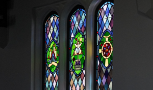 Three stained glass windows inside Good Shepherd Episcopal Church in Austin, Texas, featuring colorful Christian symbols and liturgical artwork.