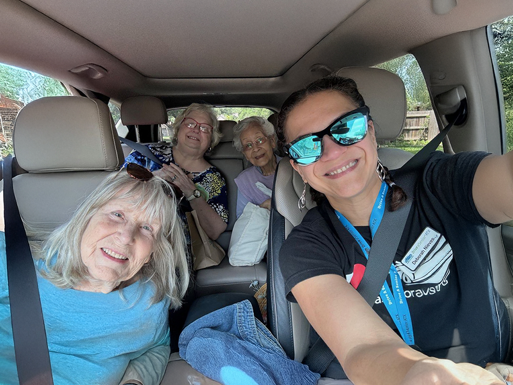 Drive-a-Senior ATX volunteer and three older adults smile together during a transportation outing in Austin, Texas.